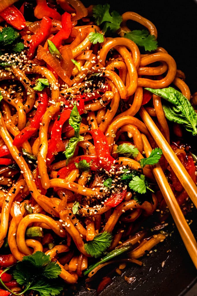 Close up of udon noodles with gochujang sauce swirled on chopsticks.