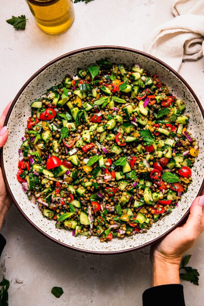 Hands holding bowl of prepared lentil tabbouleh salad.