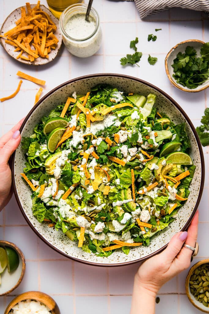 Hands holding serving bowl of prepared Mexican caesar salad.