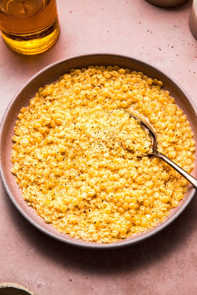 Side view of spoon dipping into bowl of parmesan pastina.