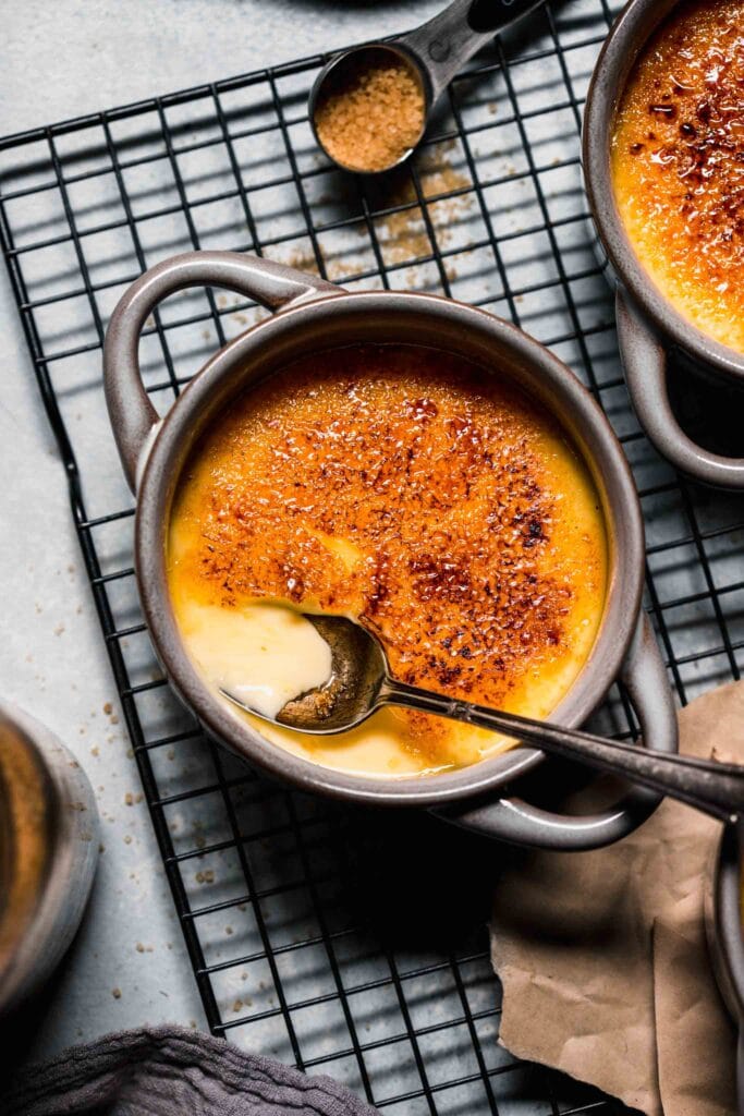 Creme brulee on cooling rack with spoon that's broken through the top.