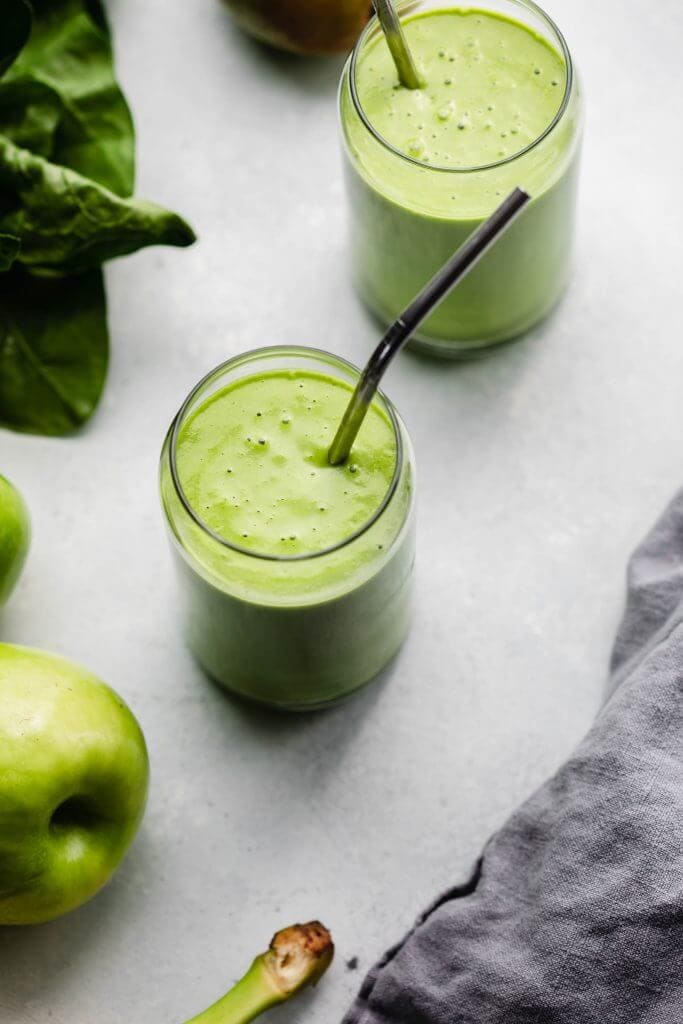 Two green smoothies on counter with metal straws.