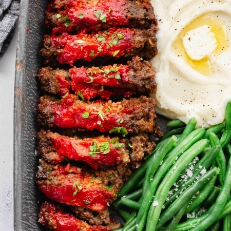 Sliced BOSTON MARKET meatloaf in serving tray with green beans and mashed potatoes.