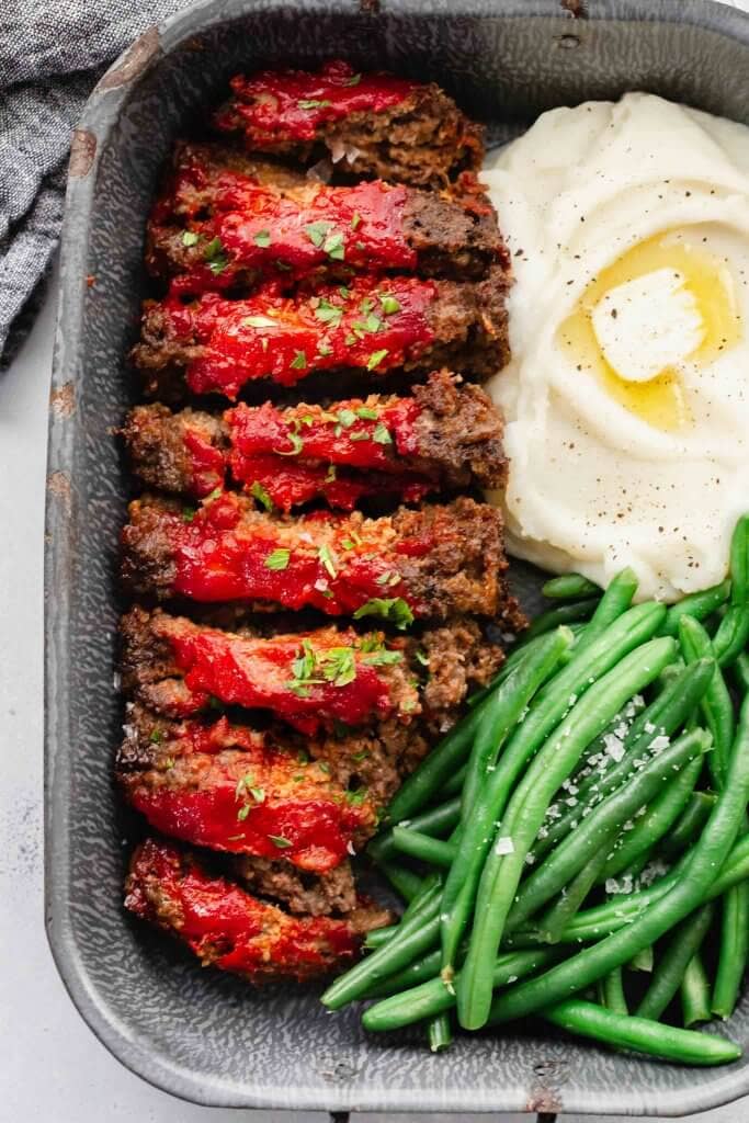 Sliced BOSTON MARKET meatloaf in serving tray with green beans and mashed potatoes.