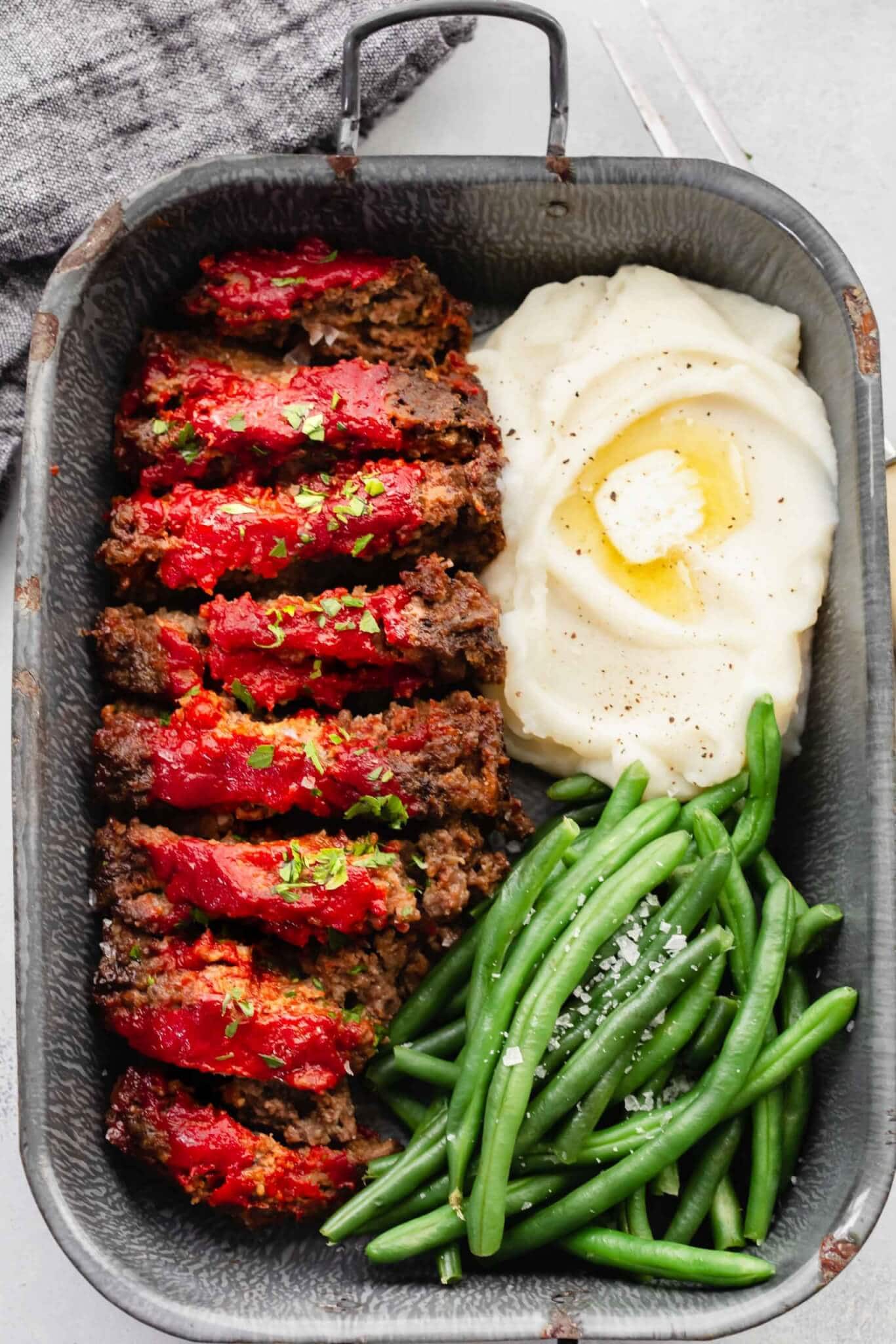 Sliced BOSTON MARKET meatloaf in serving tray with green beans and mashed potatoes.