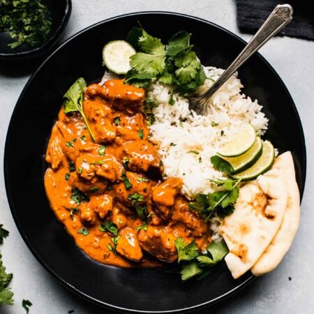 Overhead shot of slow cooker butter chicken in black bowl with rice.