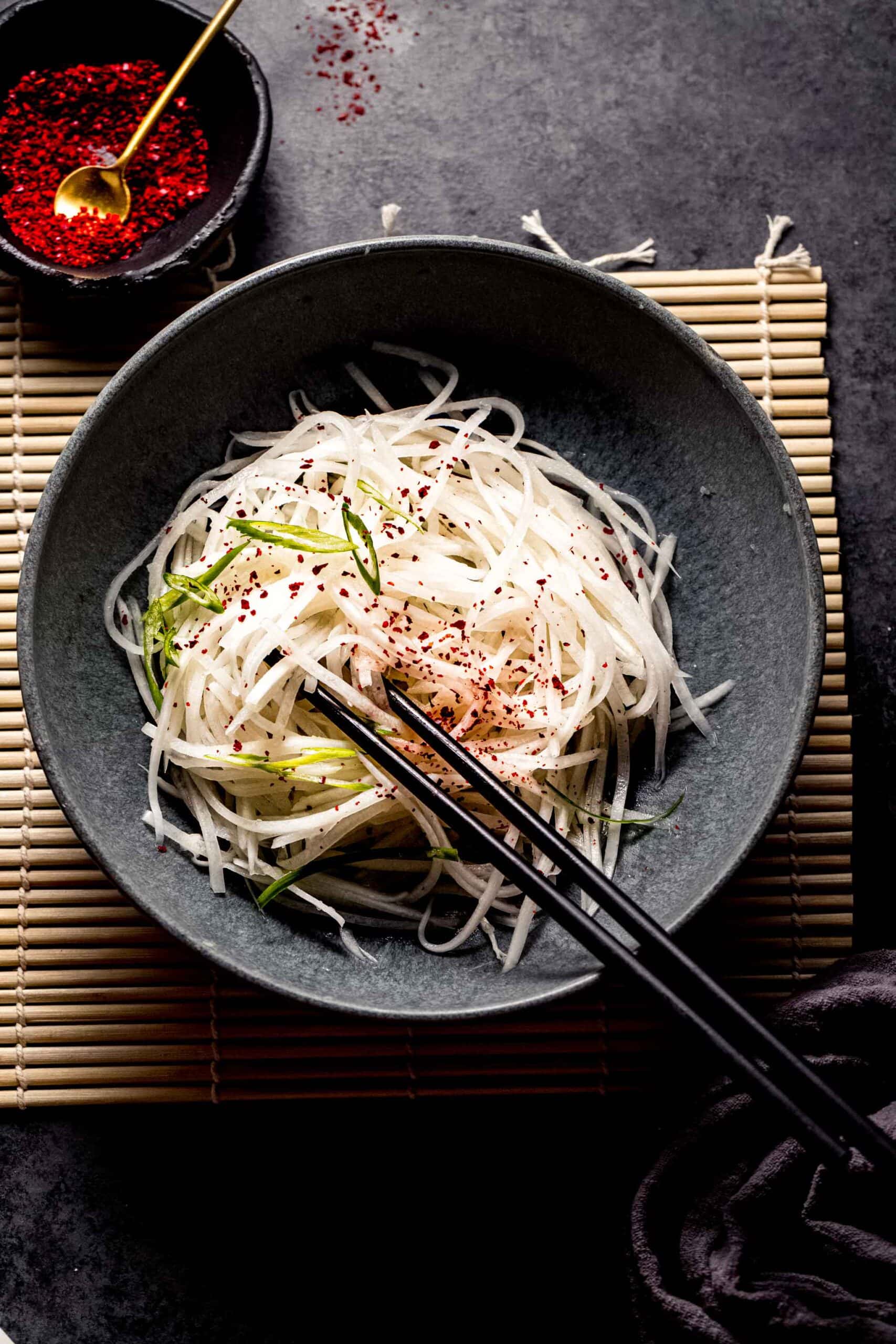 Overhead shot of daikon radish salad in grey bowl with chopsticks.