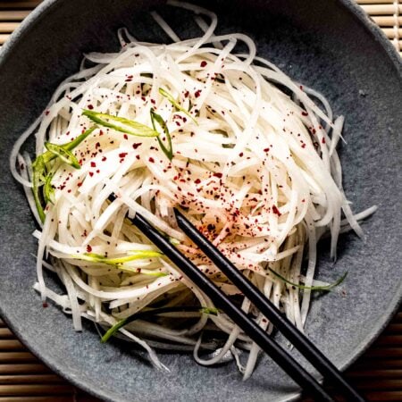 Overhead close up of daikon salad in grey bowl with chopsticks.