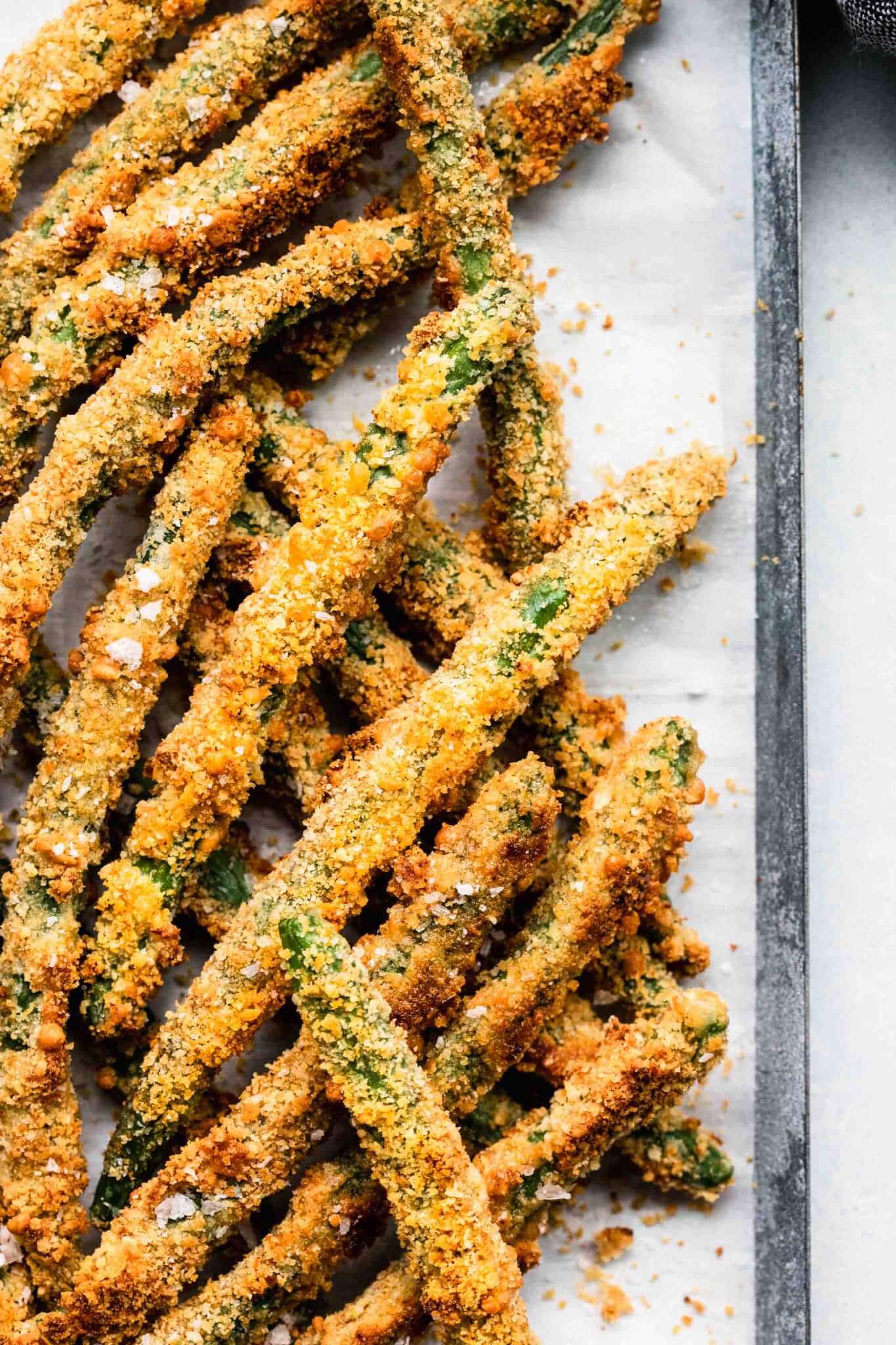 Close up of green bean fries on baking sheet lined with parchment. 