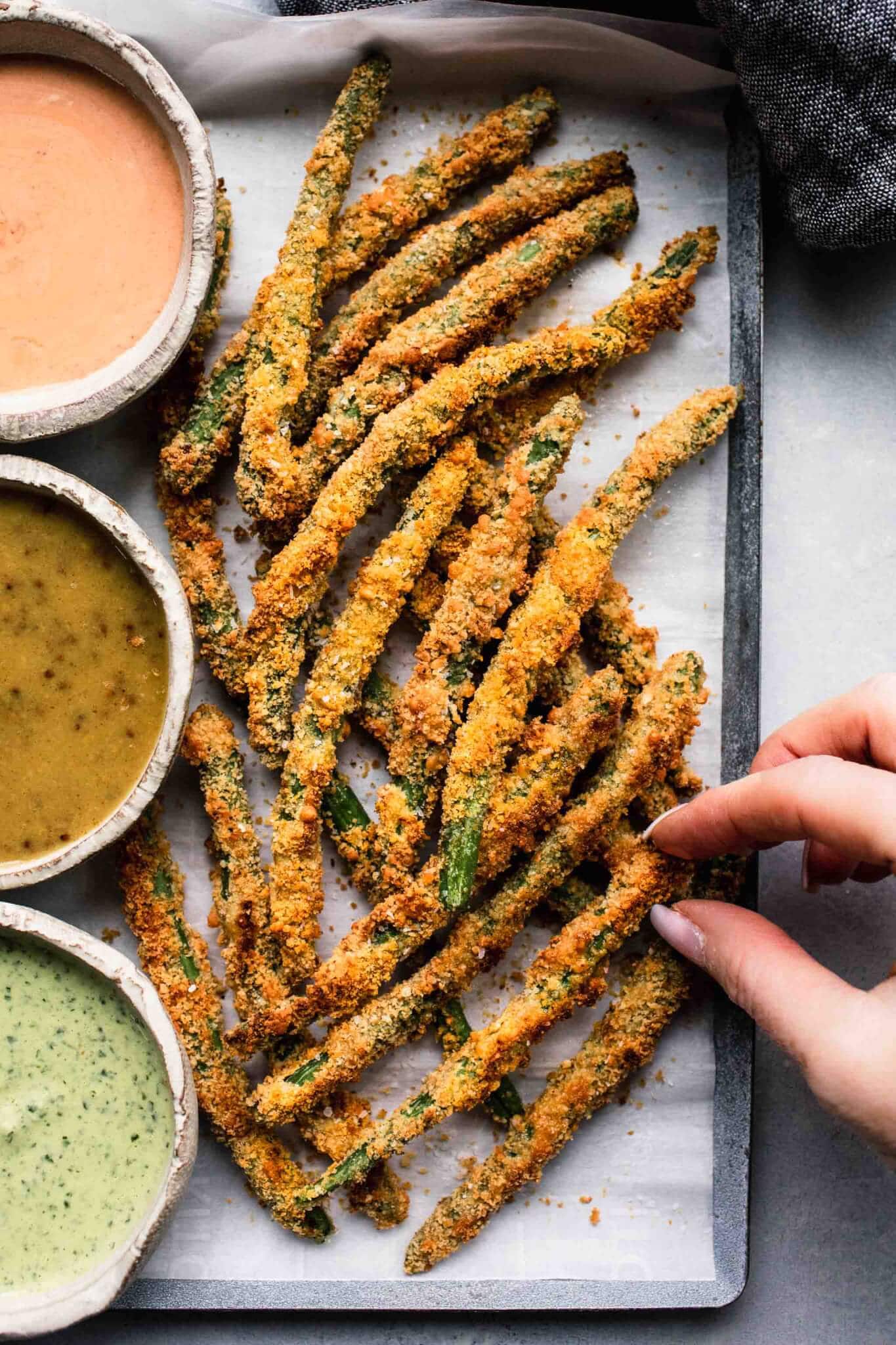 Hand taking a green bean fry off the serving tray. 