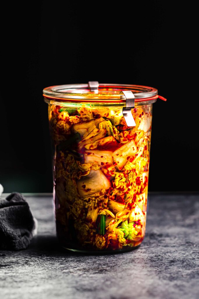 Side view of jar of kimchee with black background. 