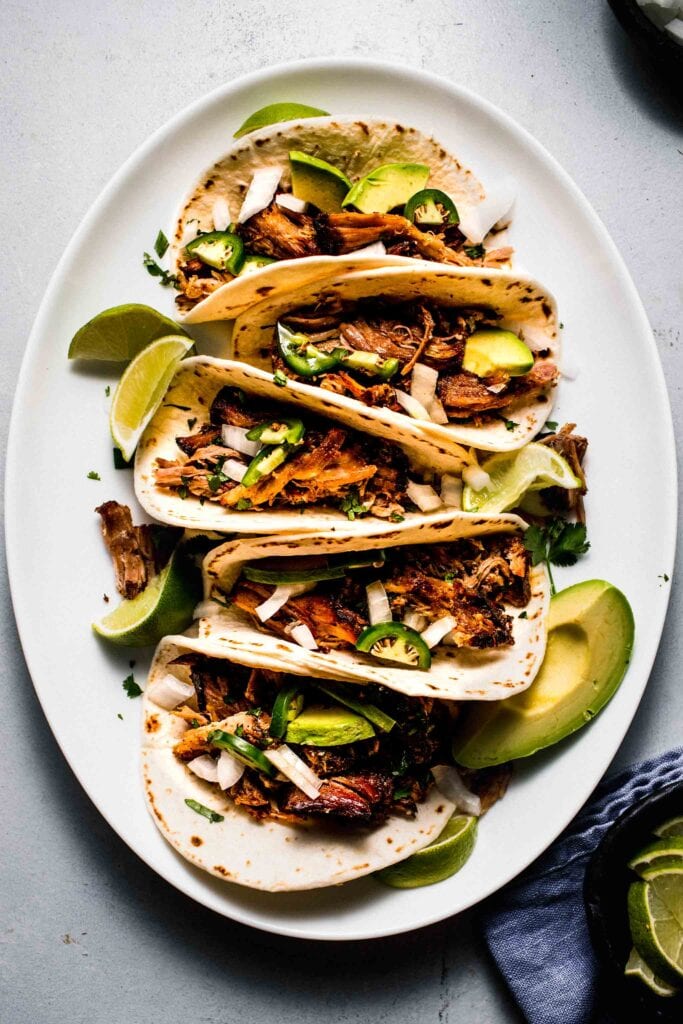 Pork street tacos arranged on white serving platter. 