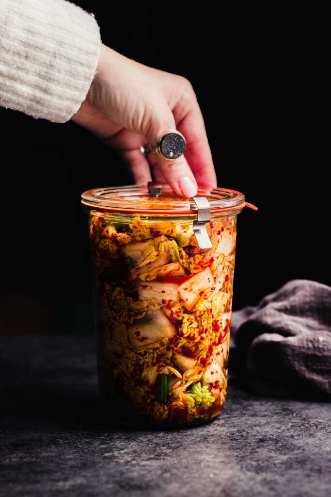 Hand holding jar of prepared kimchee. 