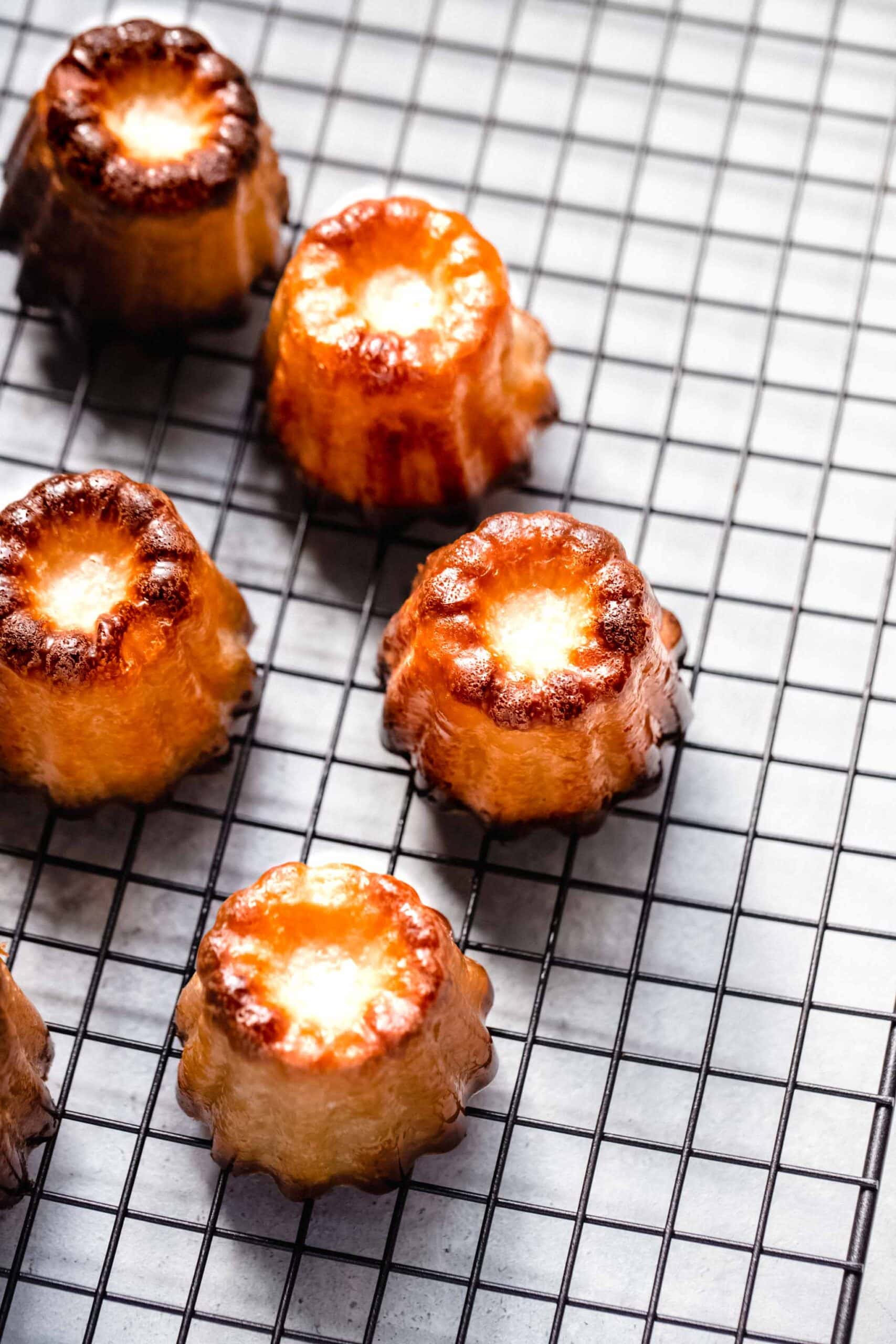 Canele cakes arranged on cooling rack.