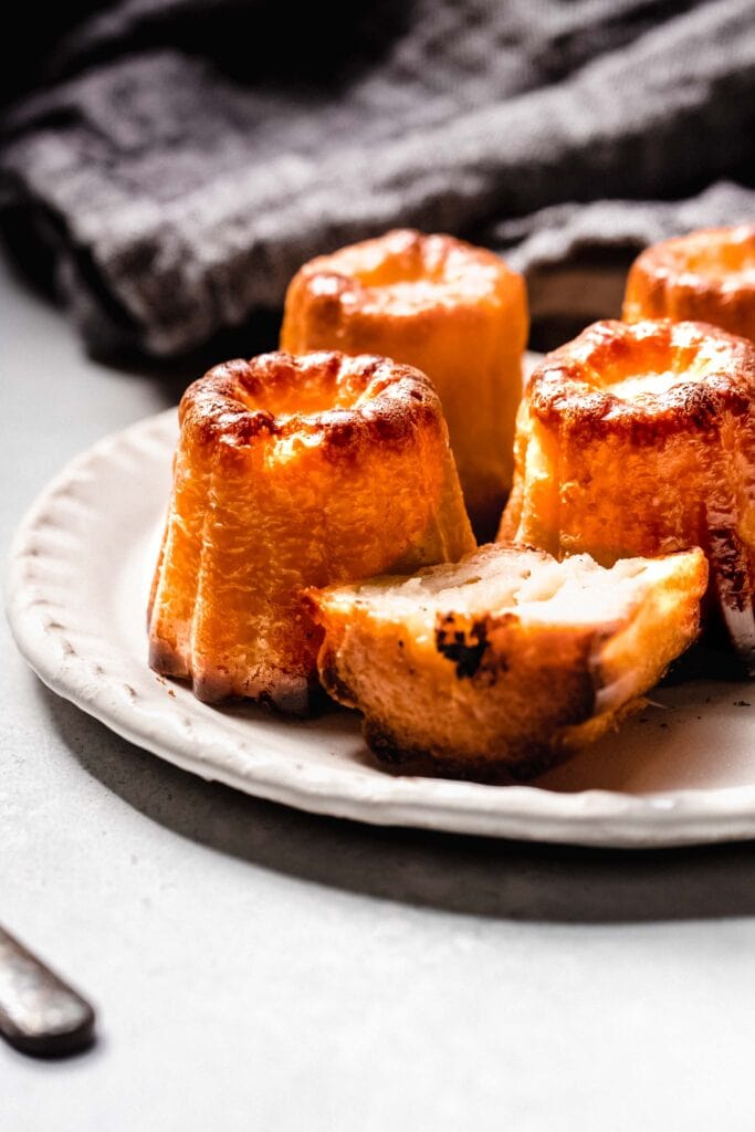 Side view of Caneles arranged on plate with one cut in half.