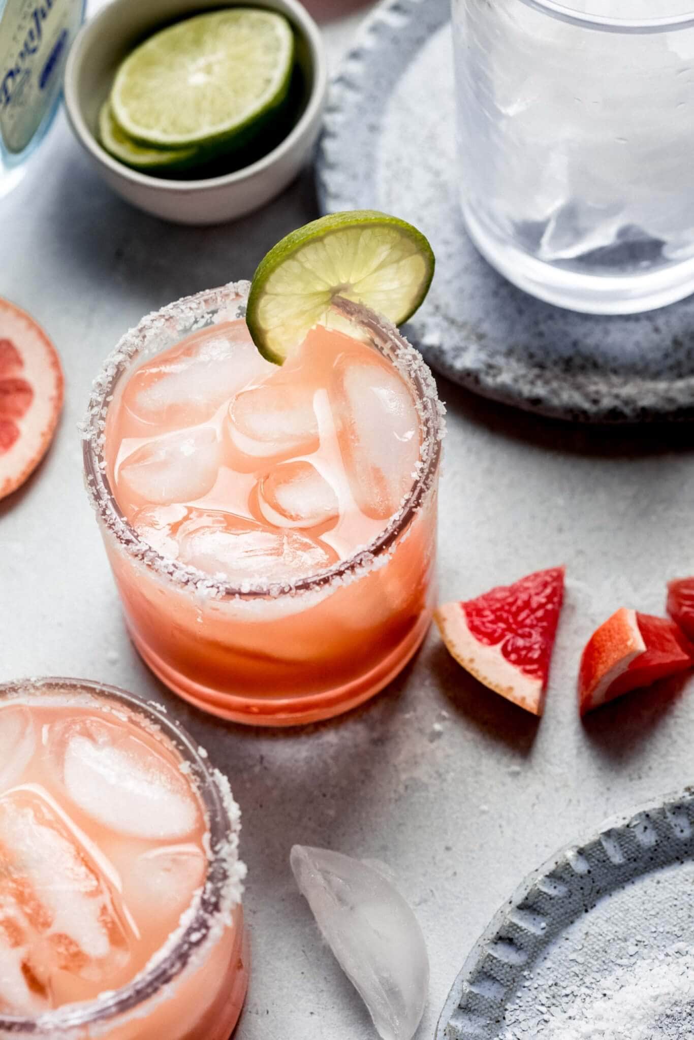 Two spicy grapefruit margaritas on counter with grapefruit and lime wedges.