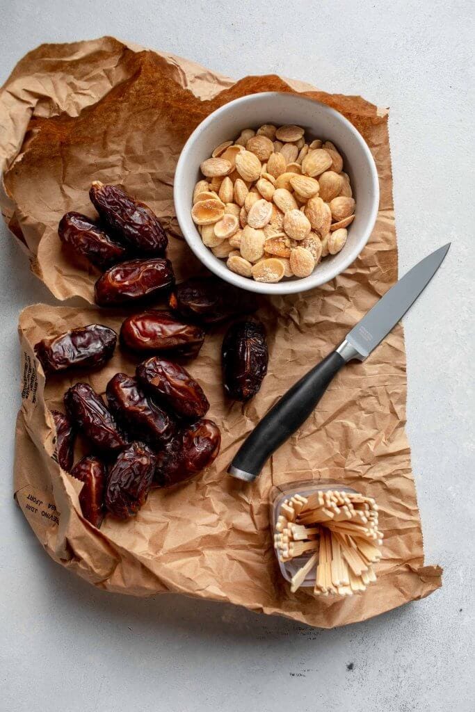 Dates on brown paper bag next to bowl of almonds.