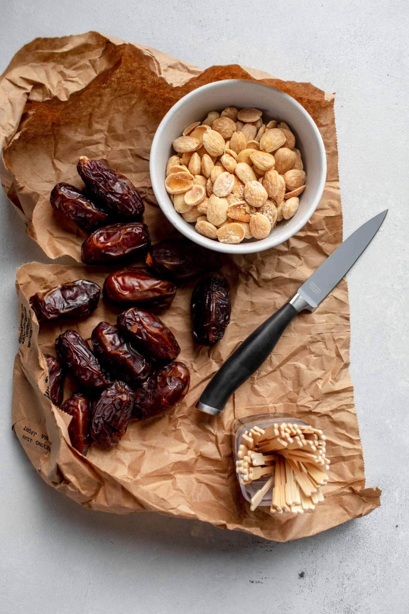 Dates on brown paper bag next to bowl of almonds. 