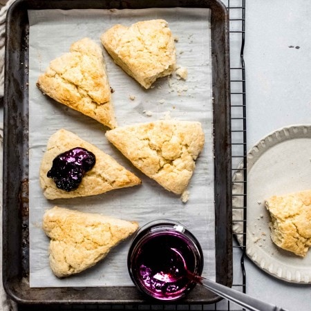 Cream scones on baking sheet next to jar of blackberry jam.