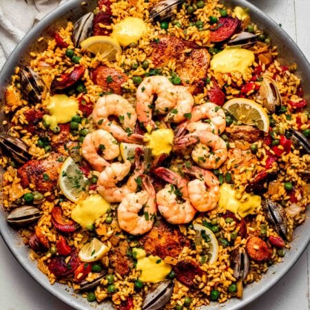 Paella in pan topped with dollops of aioli.