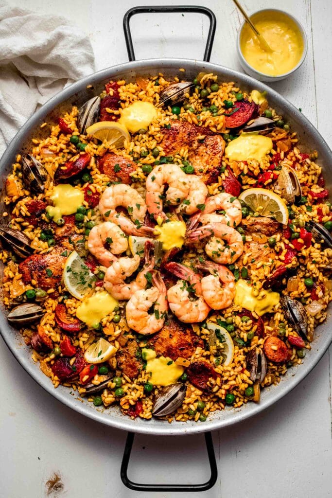 Paella in pan topped with dollops of aioli.