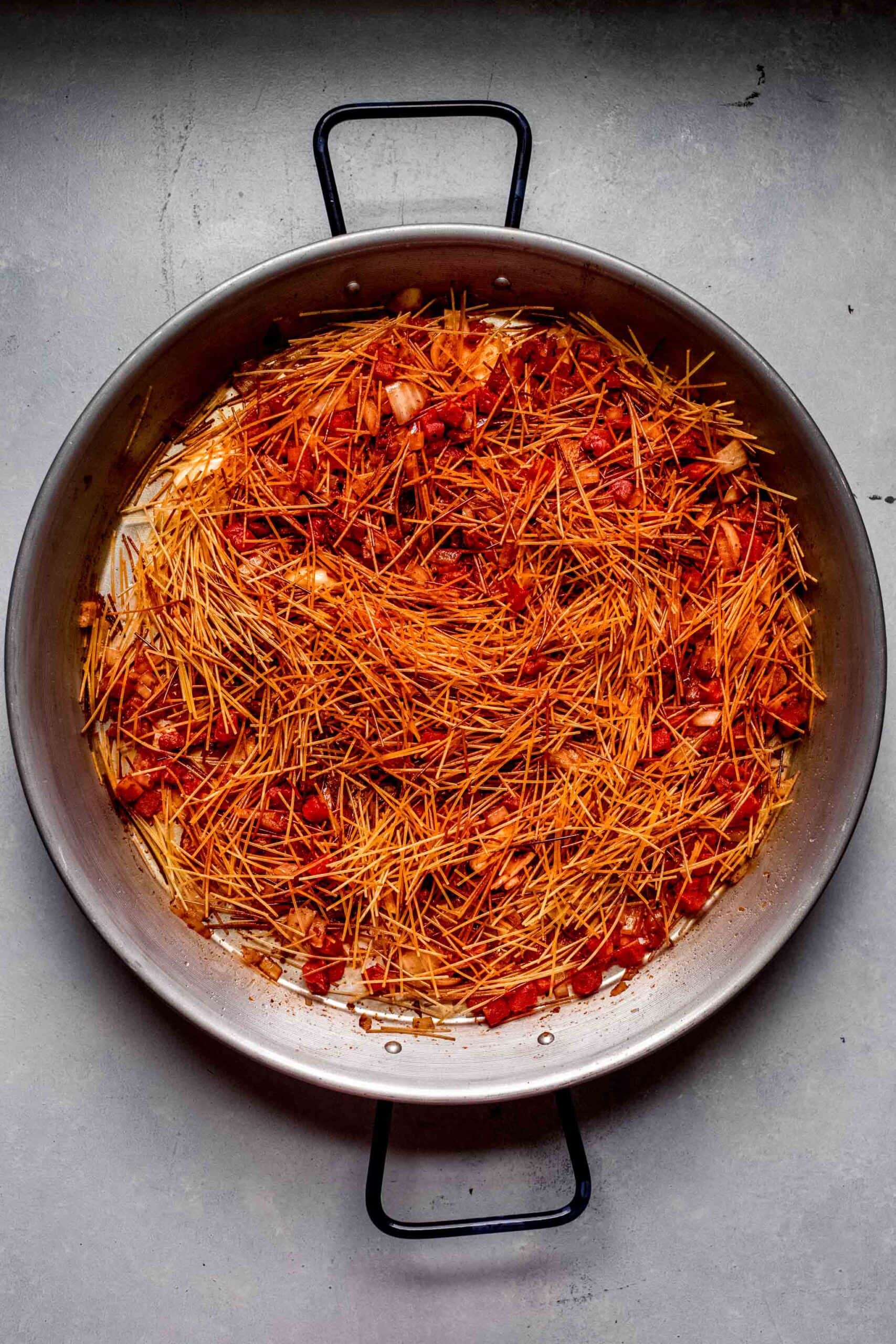 Toasted noodles tossed with tomatoes and onion in pan. 
