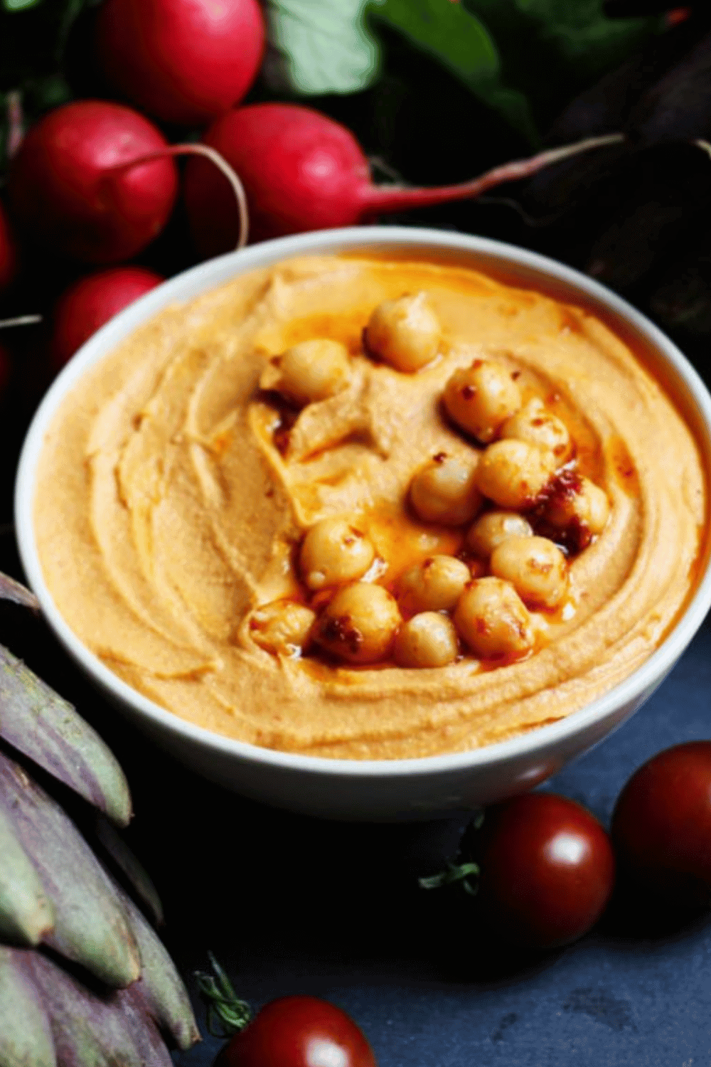 Close up of harissa hummus in bowl topped with chickpeas.