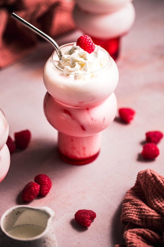 Raspberry cream italian soda in bubble glass topped with whipped cream and raspberry.