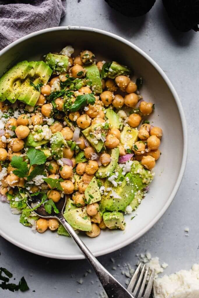 Avocado chickpea salad in a large white bowl with serving spoon.