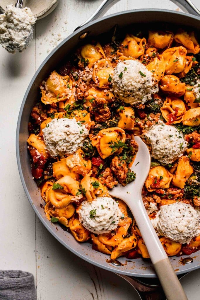 Tortellini in skillet topped with ricotta dollops. 