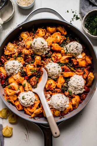 Tortellini lasagna in skillet with serving spoon.