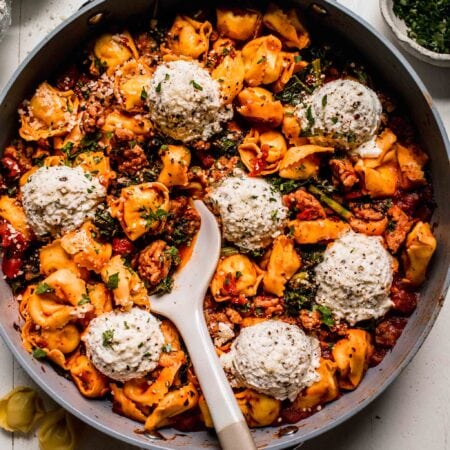 Tortellini lasagna in skillet with serving spoon.