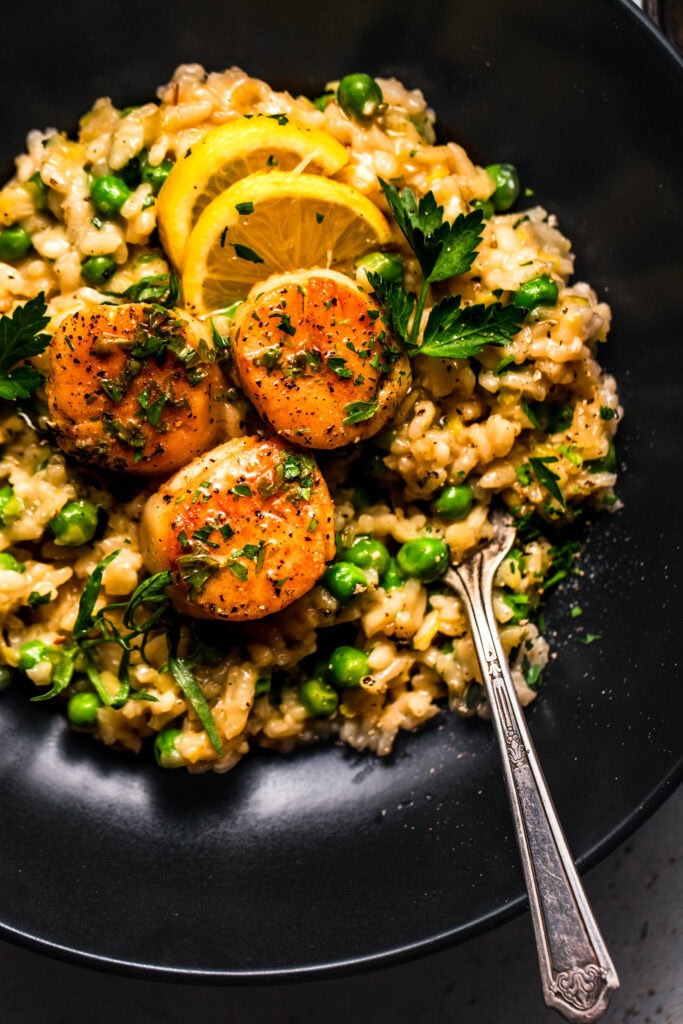 Scallop pea risotto served in black bowl. 
