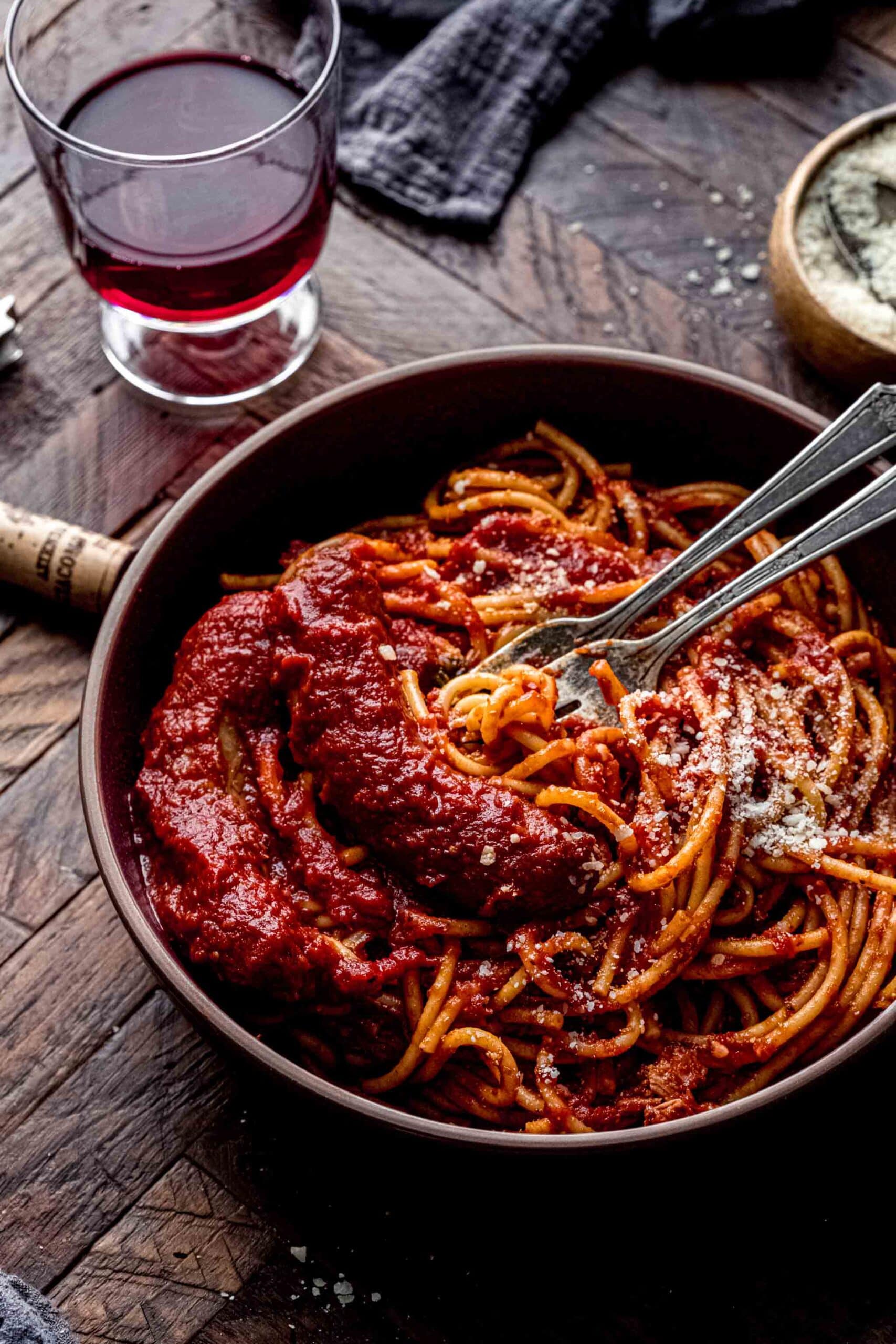 Side view of bowl of sunday sauce next to glass of wine.