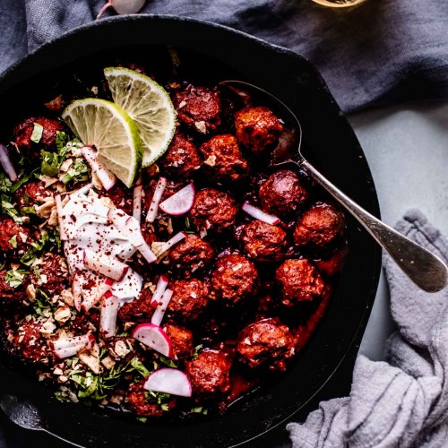 Overhead shot of mexican meatballs in skillet topped with sour cream, limes and radishes.