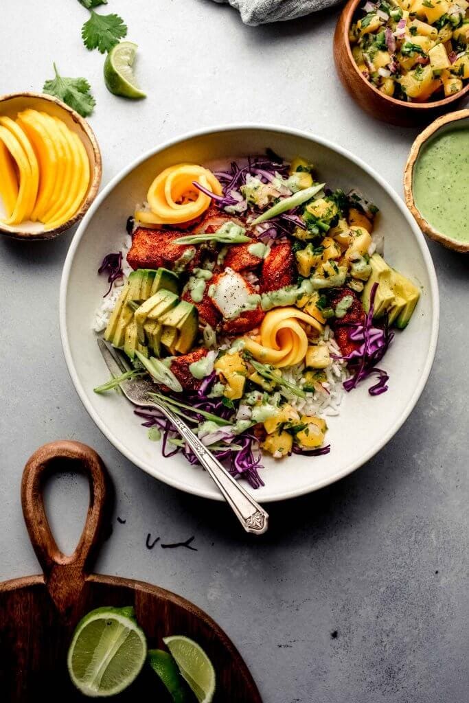 Overhead shot of fish taco bowl next to small bowls of mango salsa and avocado.