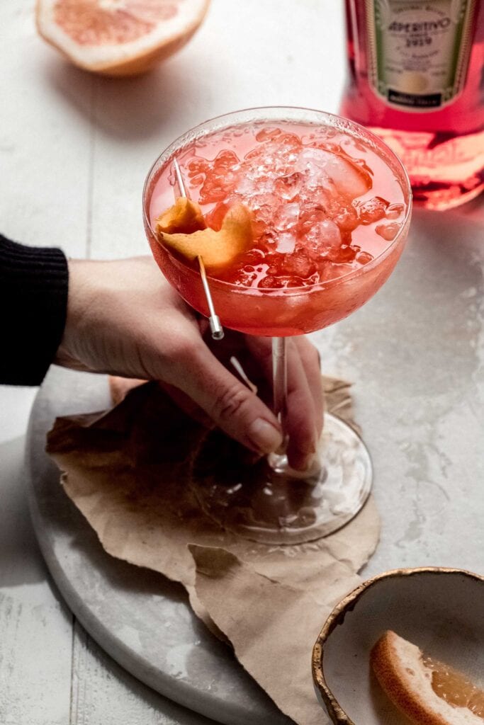 Hand holding grapefruit aperol spritz. 