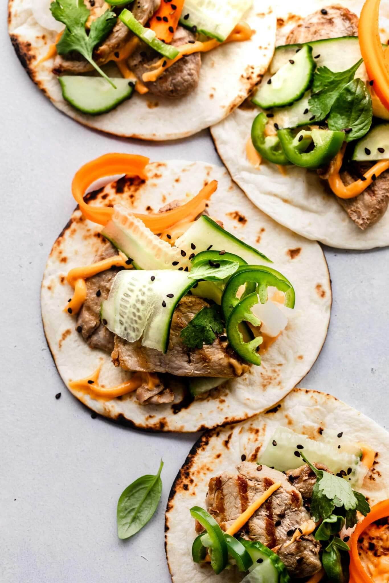 Four banh mi tacos arranged on grey slate countertop.