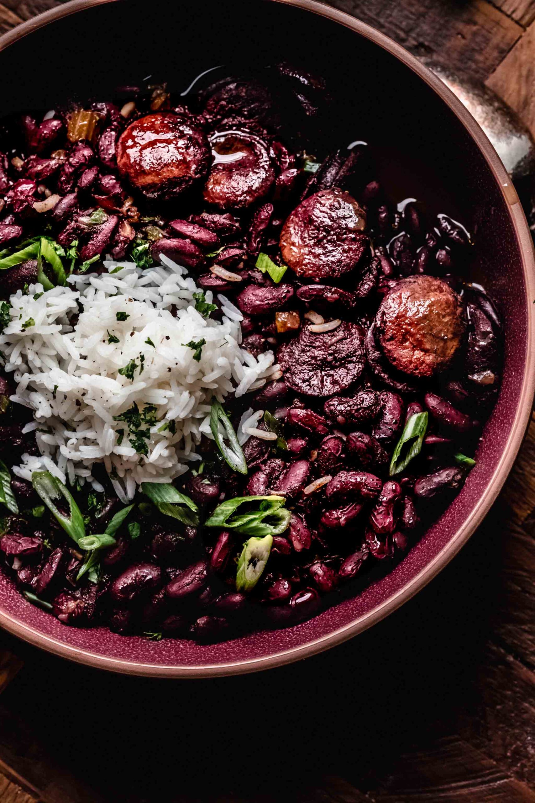 Side view of instant pot red beans & rice in maroon bowl topped with rice & green onions.