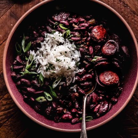 Overhead shot of red beans and sausage in red bowl topped with scoop of rice.