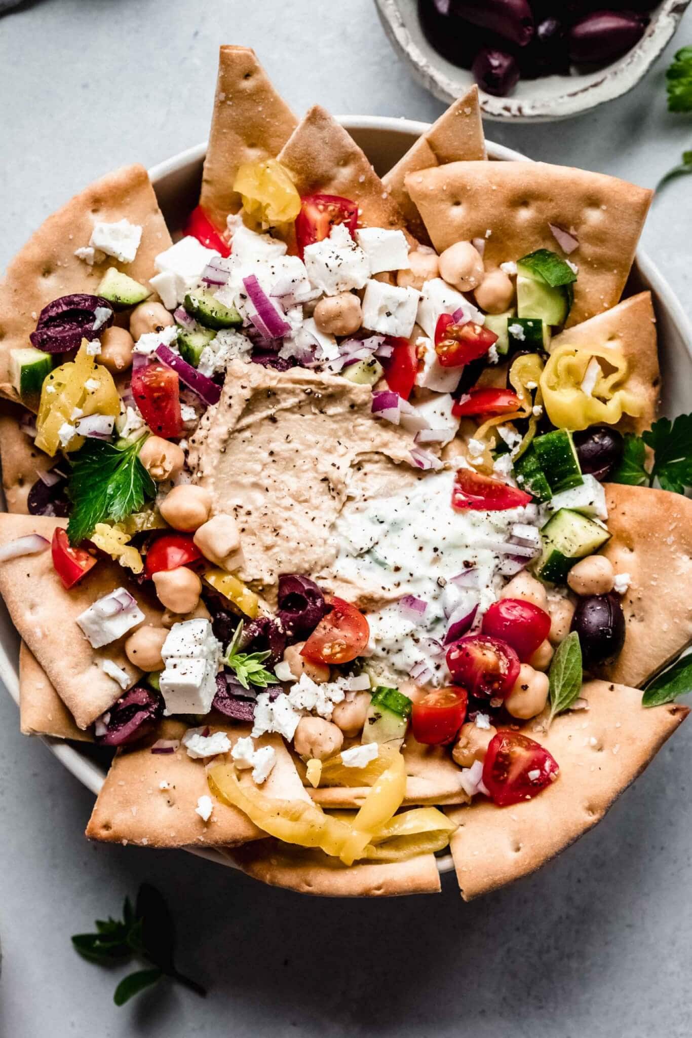 Overhead shot of greek nachos arranged on plate with toppings.