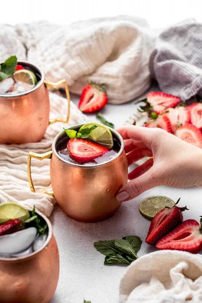 Hand holding copper mug with strawberry moscow mule inside. 