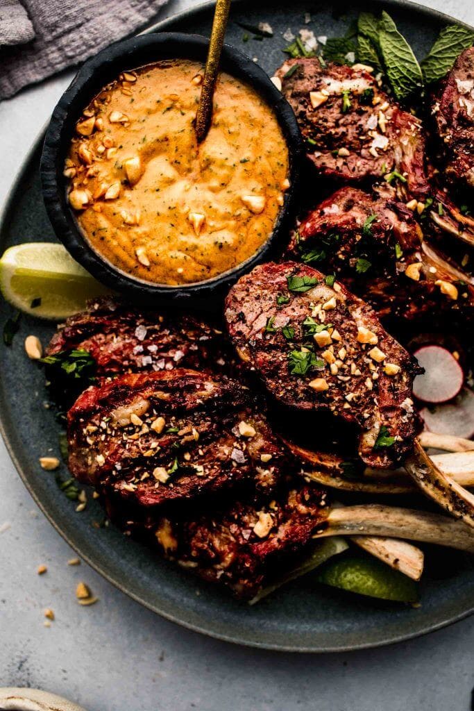 Lamb chops arranged on grey plate next to bowl of peanut sauce.