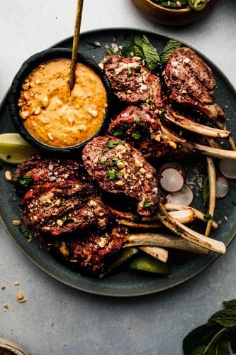 Lamb chops arranged on grey plate next to bowl of peanut sauce.