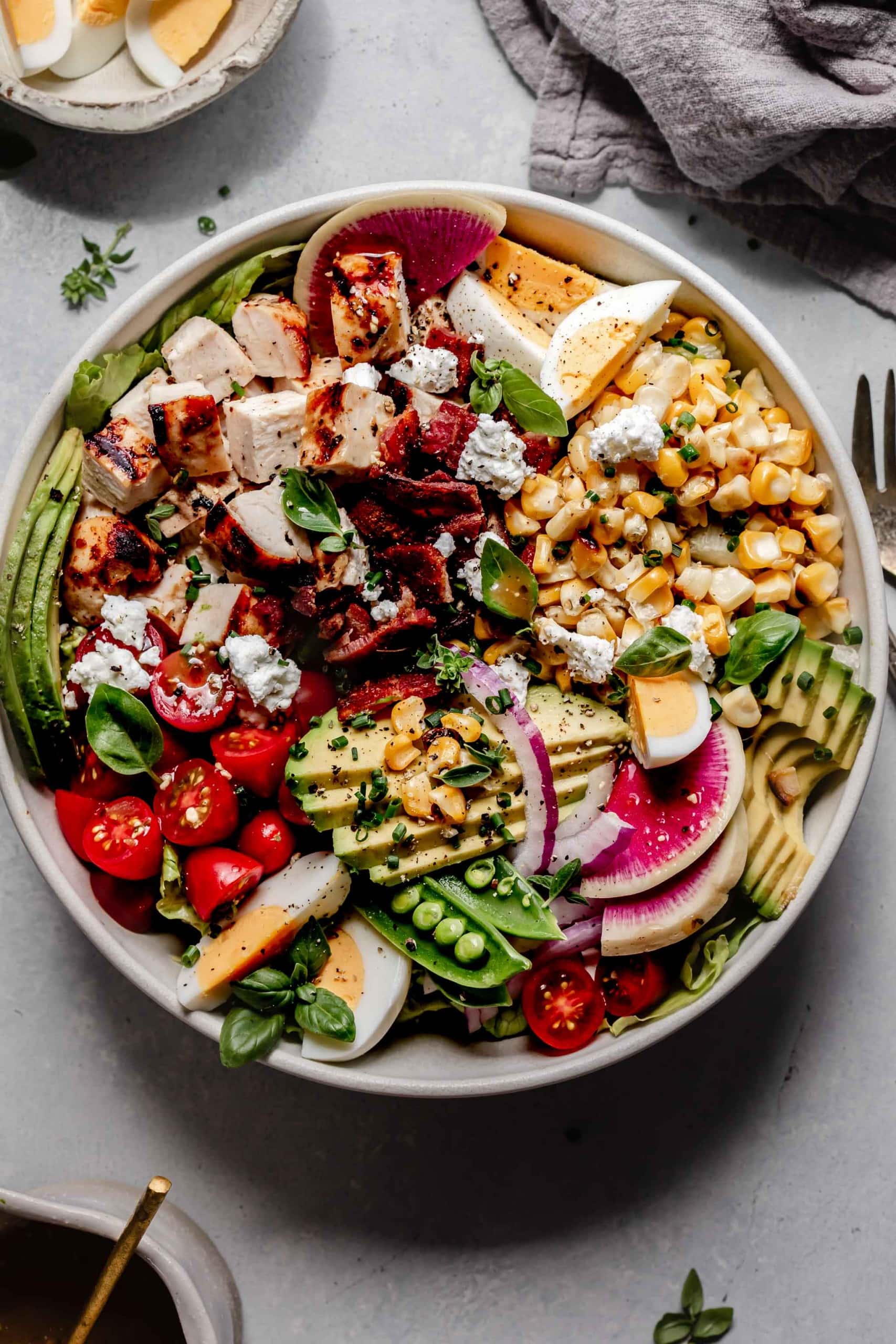 OVERHEAD SHOT OF CHICKEN COBB SALAD IN WHITE BOWL NEXT TO VINAIGRETTE.