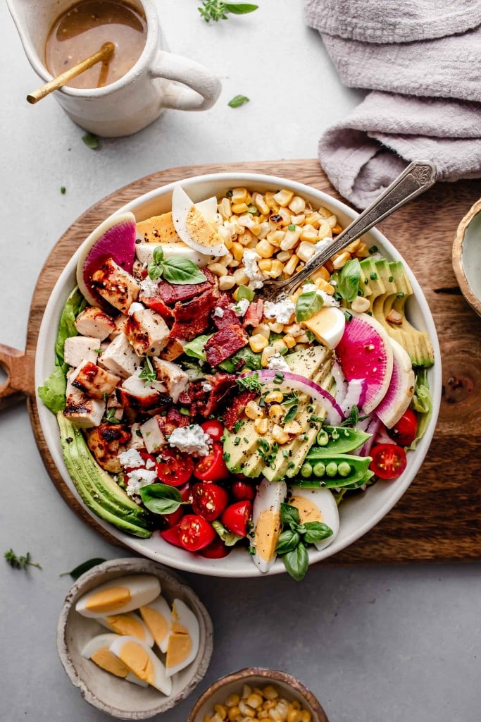 Cobb salad in bowl next to small dishes of toppings. 