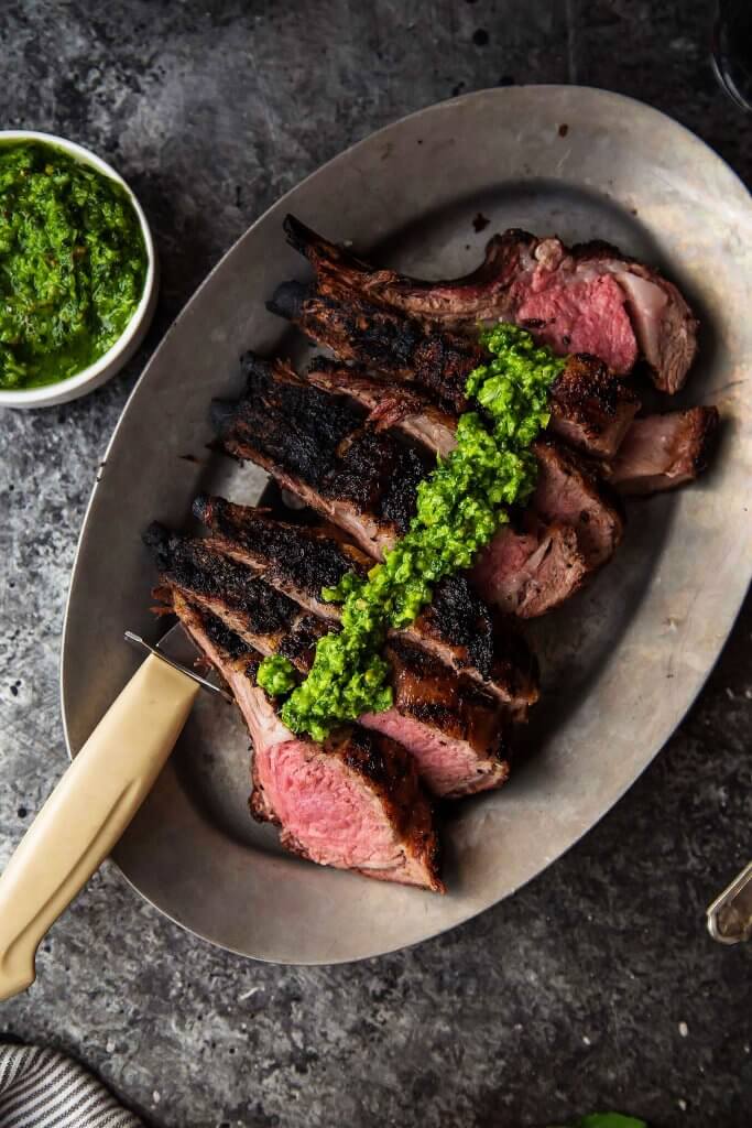 Grilled Rack of Lamb with Pistachio Basil Pesto will upgrade your next BBQ or tailgate. Frenched rack of lamb is grilled, sliced & topped with basil pesto. | platingsandpairings.com