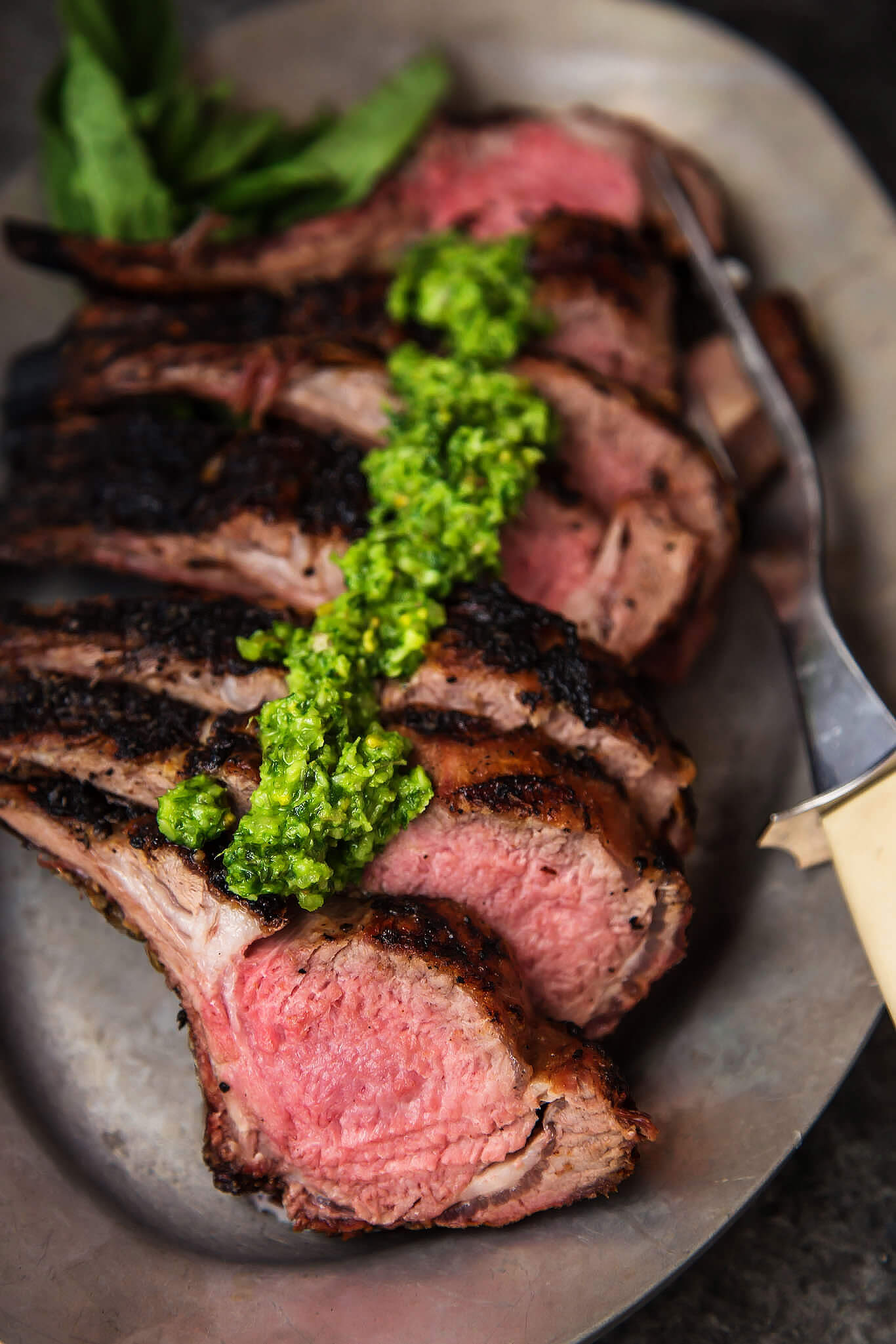 Grilled Rack of Lamb with Pistachio Basil Pesto will upgrade your next BBQ or tailgate. Frenched rack of lamb is grilled, sliced & topped with basil pesto. | platingsandpairings.com