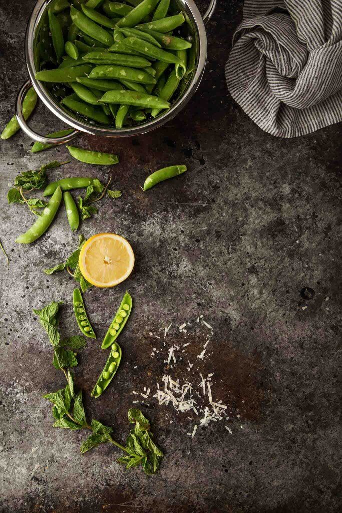 Fresh peas in colander next to lemon.