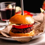 Side view of red wine burger on plate topped with tomato slice.